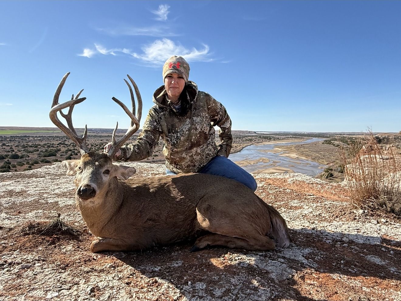 A hunter with a heavy whitetail on a rock bluff above the river