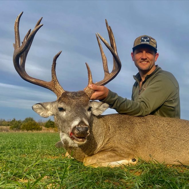 Hunter with a mature whitetail taken on a green wheat field
