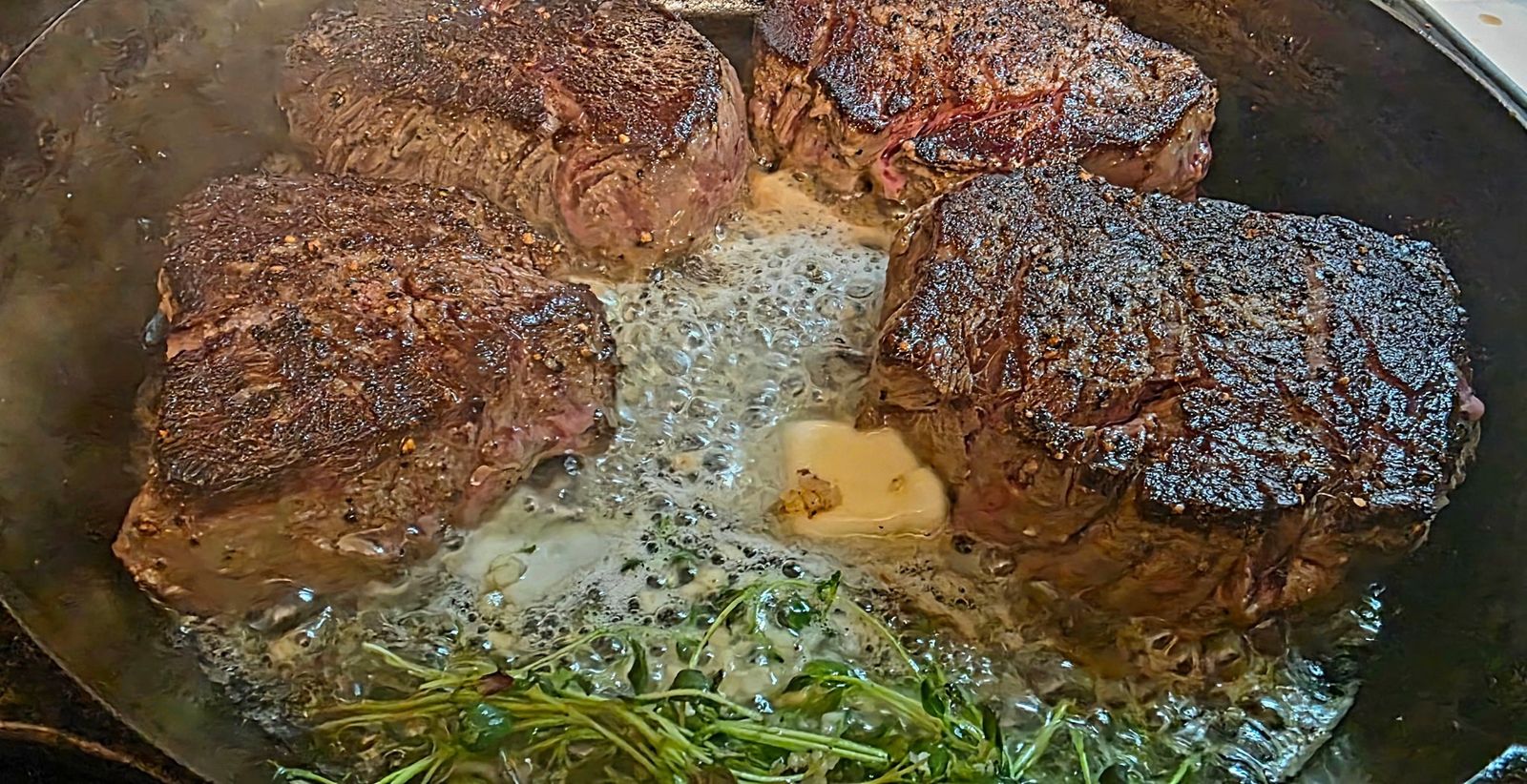 Seared steaks finishing in a cast-iron pan with butter and herbs